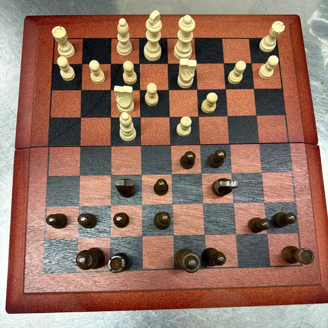Photo of a red folding wooden board from above, Black's pieces nearest the camera